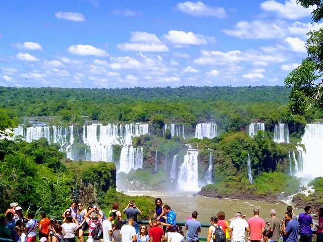 A wide view of cascading waterfalls surrounded by lush greenery with tourists.