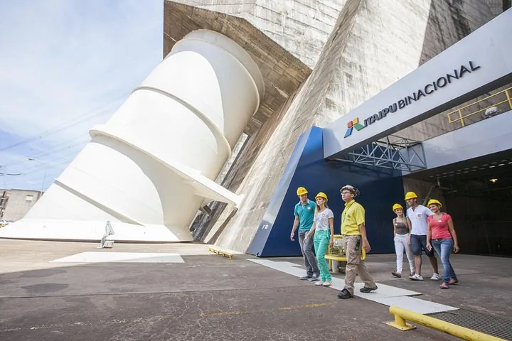 Tourists walking past a large white penstock pipe at Itaipu Dam.