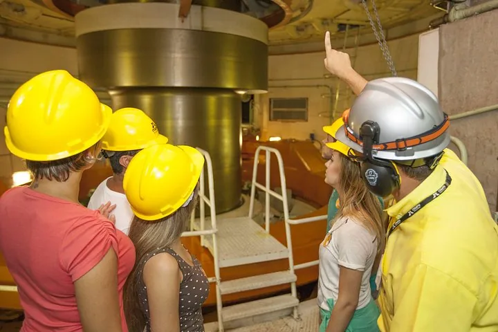 A group of tourists in hard hats looking at machinery inside a dam.