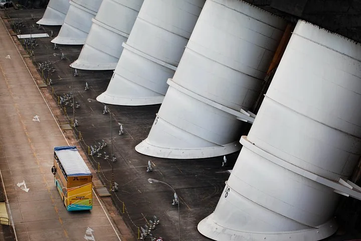 Large white penstock pipes of a dam with a tour bus passing below.