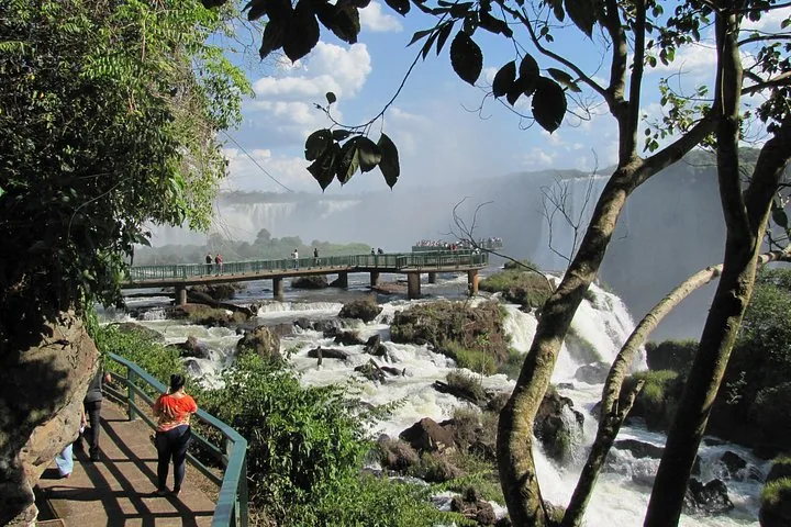 People walking on a raised viewing platform over rushing river rapids.