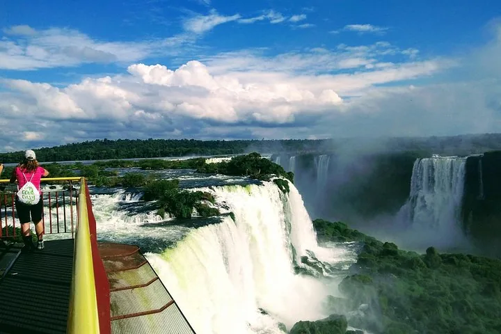 Person admiring a vast waterfall landscape from a high observation deck.